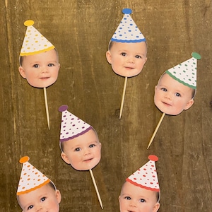K&ouml;nnte beinhalten: Sechs bunte Partyh&uuml;te mit einem Babygesicht auf jedem. Die H&uuml;te sind auf Holzst&auml;bchen und haben wei&szlig;e Punkte. Die H&uuml;te sind gelb, blau, gr&uuml;n, lila, orange und rot.