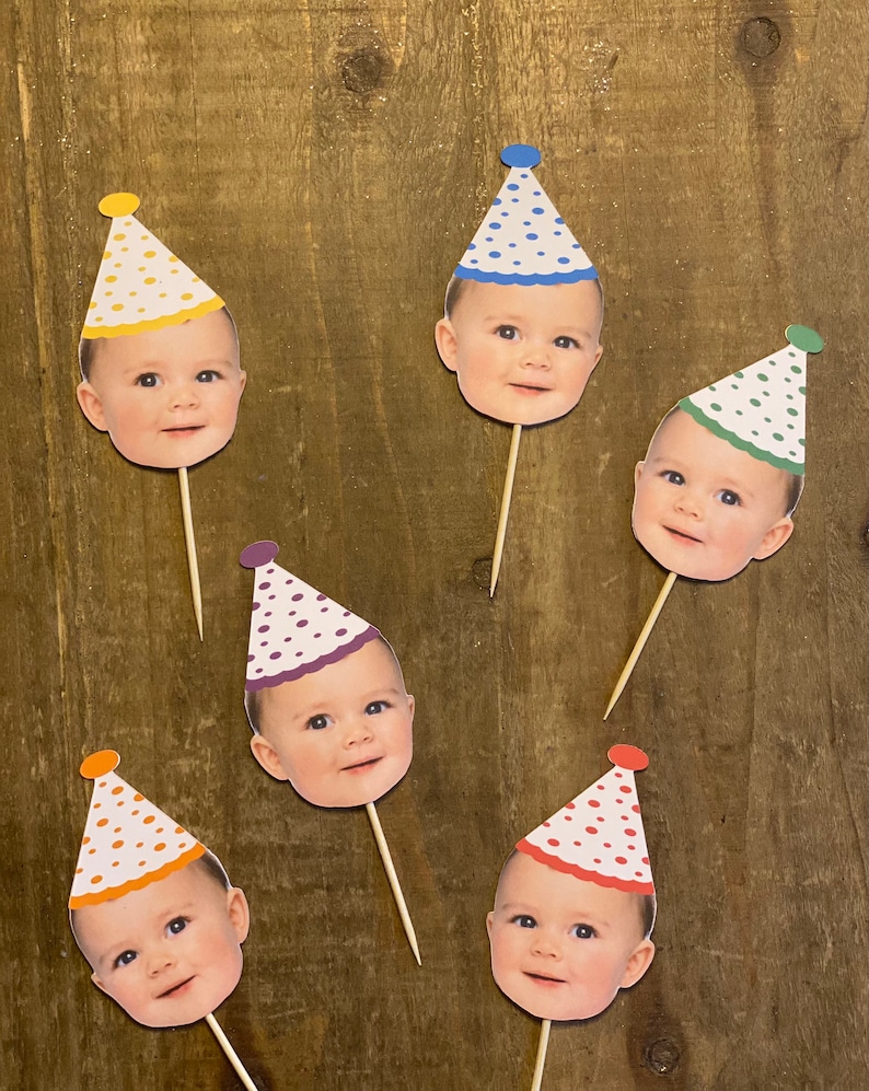 K&ouml;nnte beinhalten: Sechs bunte Partyh&uuml;te mit einem Babygesicht auf jedem. Die H&uuml;te sind auf Holzst&auml;bchen und haben wei&szlig;e Punkte. Die H&uuml;te sind gelb, blau, gr&uuml;n, lila, orange und rot.