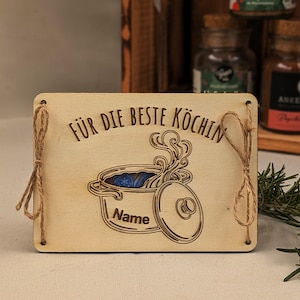 Può includere: Cartello in legno chiaro con la scritta "FÜR DIE BESTE KÖCHIN" e un disegno di pentola. Il cartello è decorato con corda e presenta la parola "Name" sotto la pentola. Ideale per la cucina.