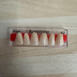 May include: A close-up of a dental shade guide with six teeth samples labeled "PW6" and "62". The guide is labeled "Acrotone" and is made of plastic.