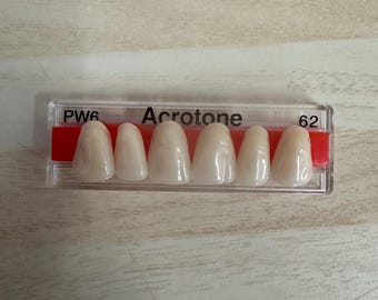 May include: A close-up of a dental shade guide with six teeth samples labeled "PW6" and "62". The guide is labeled "Acrotone" and is made of plastic.