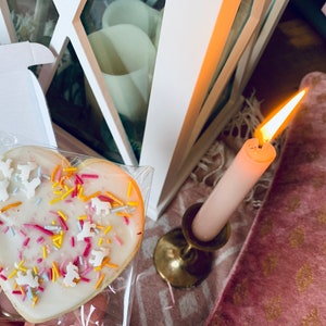 Puede incluir: Una galleta de az&uacute;car en forma de coraz&oacute;n decorada con glaseado blanco y chispas de colores. La galleta est&aacute; en una bolsa de pl&aacute;stico transparente y est&aacute; sobre una superficie blanca.