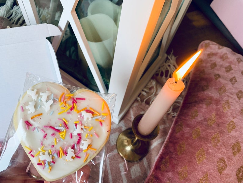 Puede incluir: Una galleta de az&uacute;car en forma de coraz&oacute;n decorada con glaseado blanco y chispas de colores. La galleta est&aacute; en una bolsa de pl&aacute;stico transparente y est&aacute; sobre una superficie blanca.