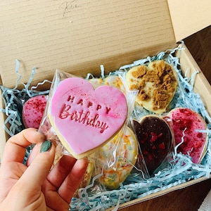 Puede incluir: Una caja de regalo llena de galletas en forma de coraz&oacute;n de color rosa, rojo y blanco. Una galleta tiene las palabras "Happy Birthday" escritas en glaseado rosa.