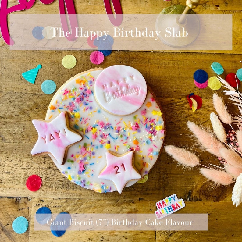 Pu&ograve; includere: Un grande biscotto rotondo bianco decorato con glassa rosa e codette colorate. Il biscotto ha una stella di glassa rosa con la parola "YAY!" su di essa, una stella di glassa rosa con il numero "21" su di essa e un cerchio di glassa rosa con le parole "HAPPY BIRTHDAY" su di esso. Il biscotto &egrave; su una superficie di legno con coriandoli colorati sparsi intorno. Il testo "Giant Biscuit (7") Birthday Cake Flavour" &egrave; nella parte inferiore dell'immagine.