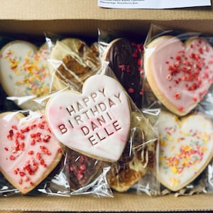 Puede incluir: Una caja llena de galletas con forma de coraz&oacute;n decoradas con chispas, glaseado y el mensaje "Happy Birthday Dani Elle".