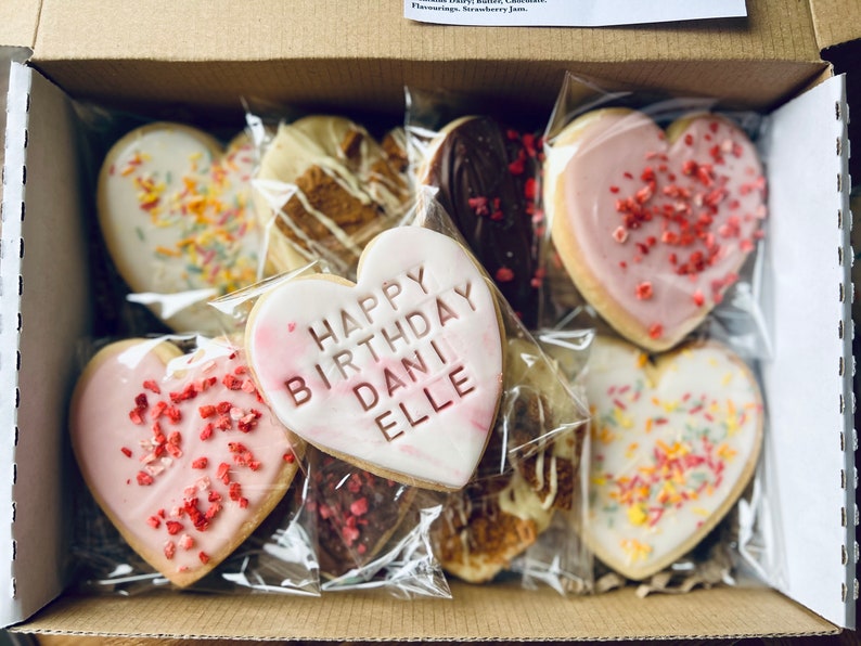 Puede incluir: Una caja llena de galletas con forma de coraz&oacute;n decoradas con chispas, glaseado y el mensaje "Happy Birthday Dani Elle".
