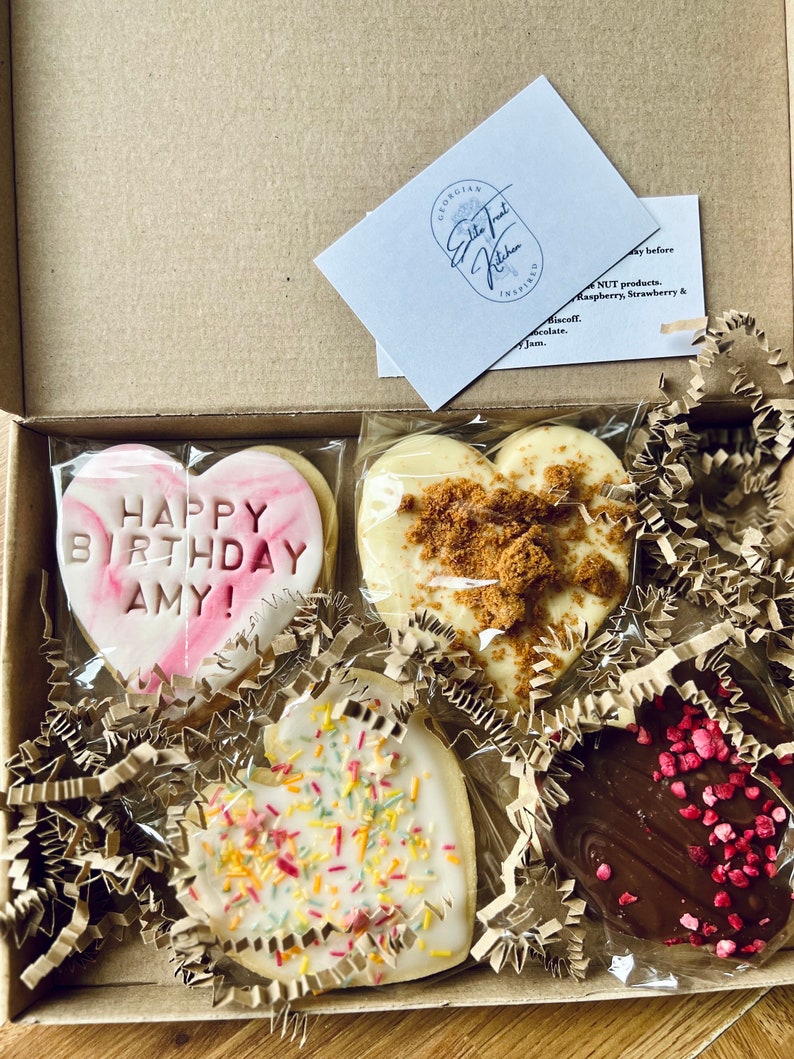 Puede incluir: Una caja de regalo llena de cuatro galletas con forma de coraz&oacute;n. Las galletas est&aacute;n decoradas con chispas, glaseado y un mensaje que dice "&iexcl;Feliz cumplea&ntilde;os Amy!"