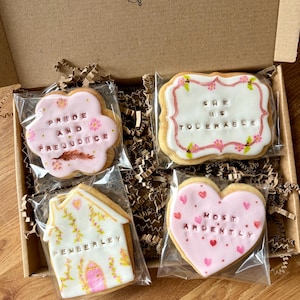 May include: Four individually wrapped sugar cookies in a cardboard box. One flower-shaped cookie says PRIDE AND PREJUDICE, a rectangular one says SHE IS TOLERABLE, a house-shaped one says PEMBERLEY, and a heart-shaped one says MOST ARDENTLY.