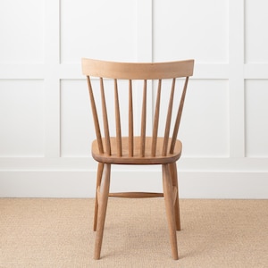 May include: A wooden chair with a light brown finish and a slatted back. The chair has a simple design with a curved back and four legs.