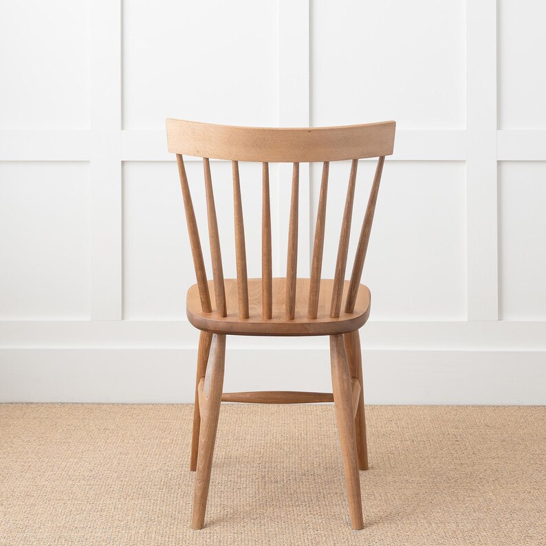 May include: A wooden chair with a light brown finish and a slatted back. The chair has a simple design with a curved back and four legs.