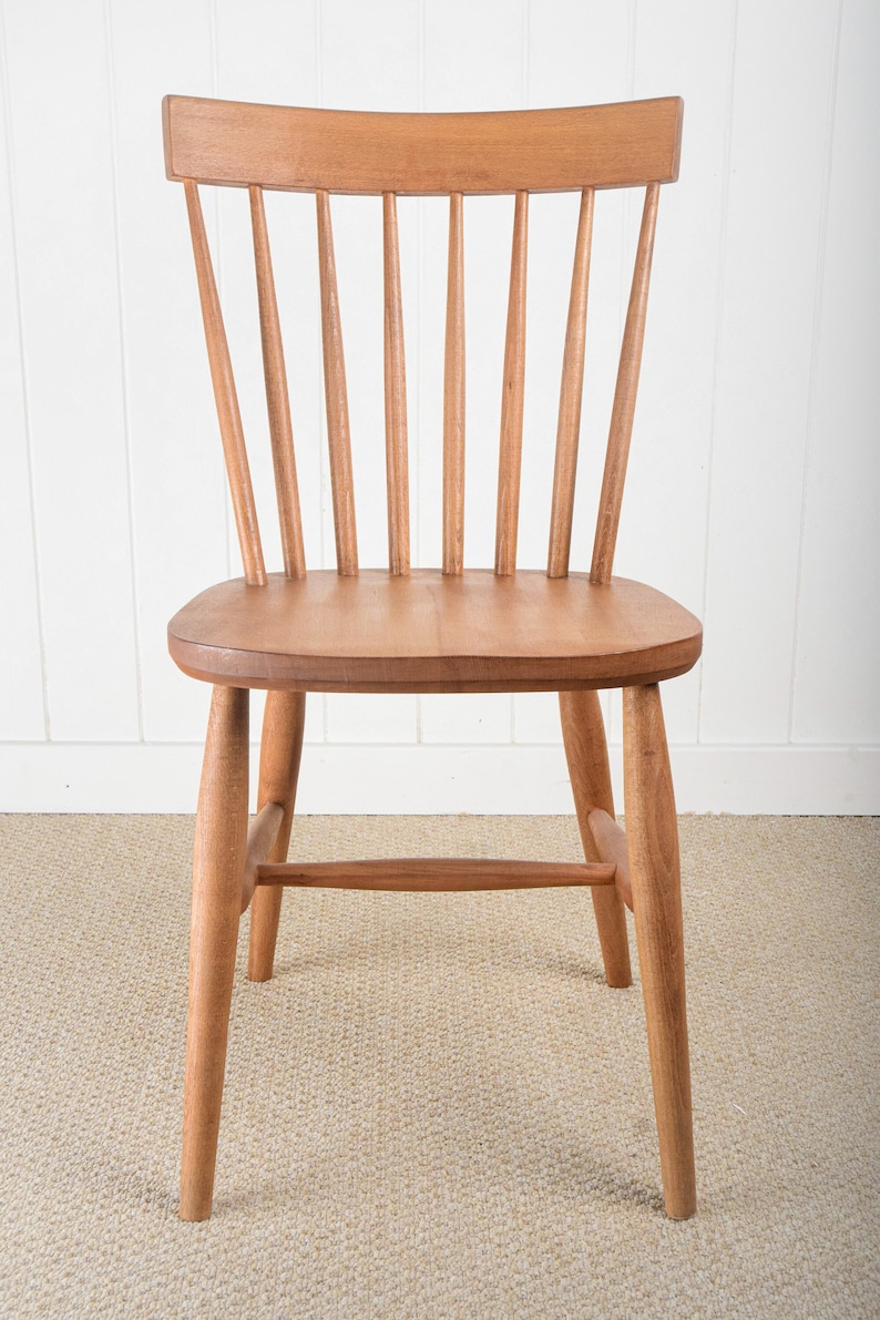 May include: A wooden chair with a light brown finish. The chair has a slatted back and a curved seat. The chair is sitting on a beige carpet.