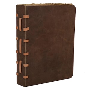 May include: A brown leather journal with a textured cover. The spine is stitched with tan leather strips. The pages have a rough, aged appearance, suggesting a vintage or handcrafted style.