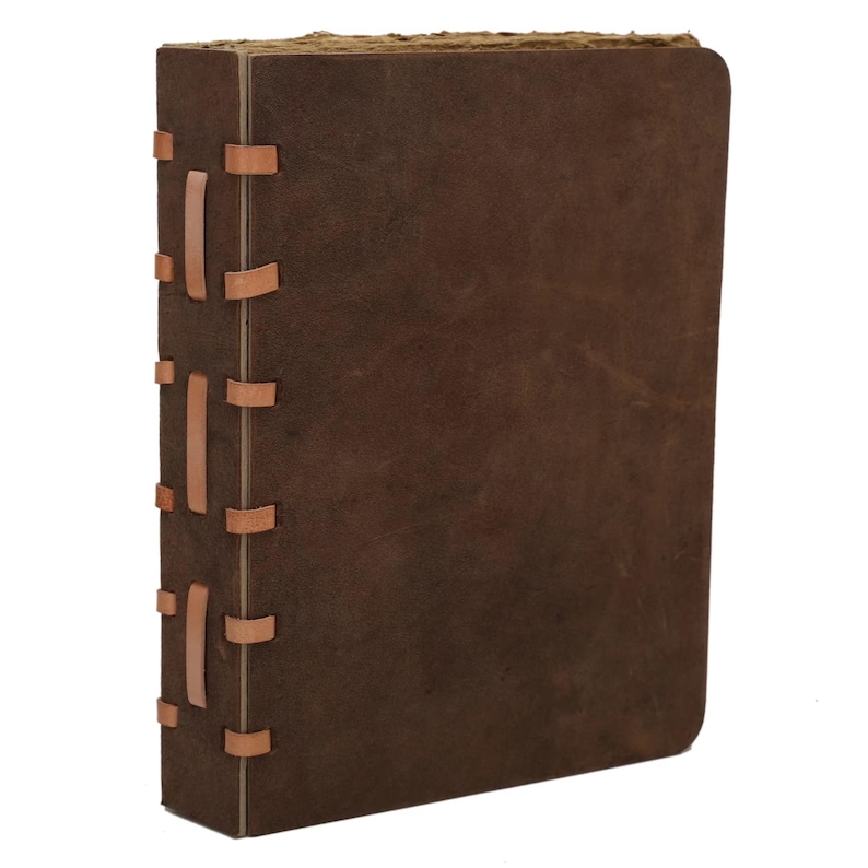 May include: A brown leather journal with a textured cover. The spine is stitched with tan leather strips. The pages have a rough, aged appearance, suggesting a vintage or handcrafted style.