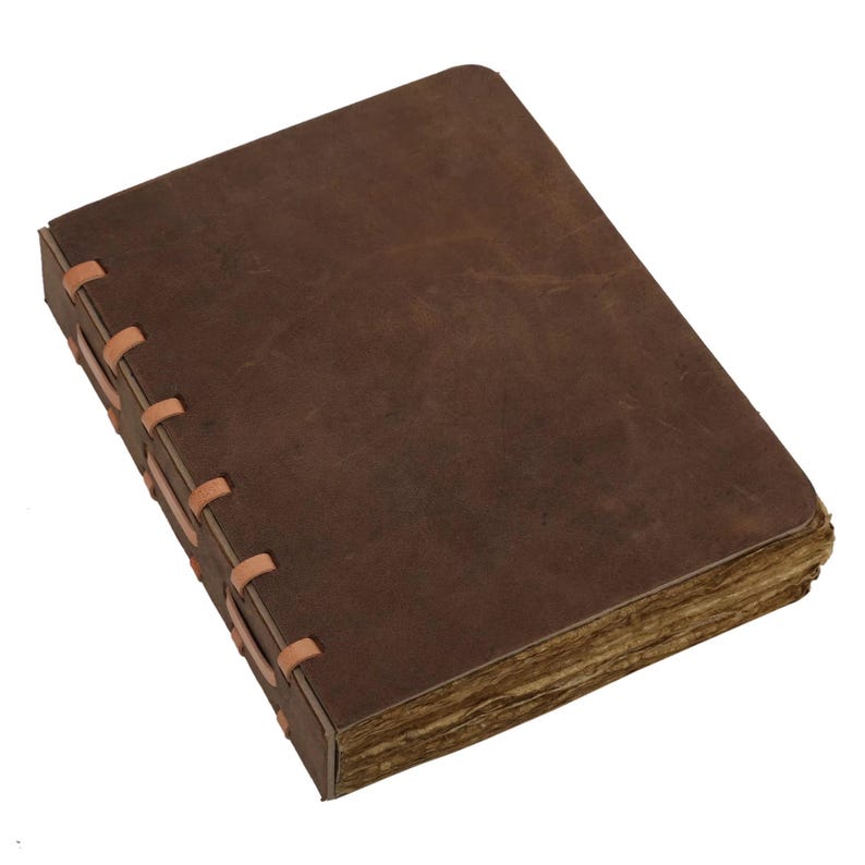 May include: A brown leather journal with a rectangular shape and a distressed look. The pages have an aged appearance, and the spine is hand-stitched with tan thread. The journal is closed, ready for use.
