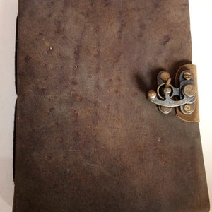 May include: A brown leather journal with a brass clasp closure. The journal has a distressed look and is perfect for writing or sketching.