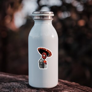 May include: A white stainless steel water bottle with a sticker of a cartoon superhero wearing a sombrero. The superhero is red and black with a white mask.