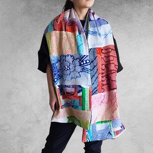 以下が含まれることがあります： 赤、青、緑、ピンクなど、さまざまな模様と色を使ったカラフルなパッチワークのスカーフ。 黒いトップスと黒いパンツを着た人に巻かれています。 スカーフは織物で作られているようです。