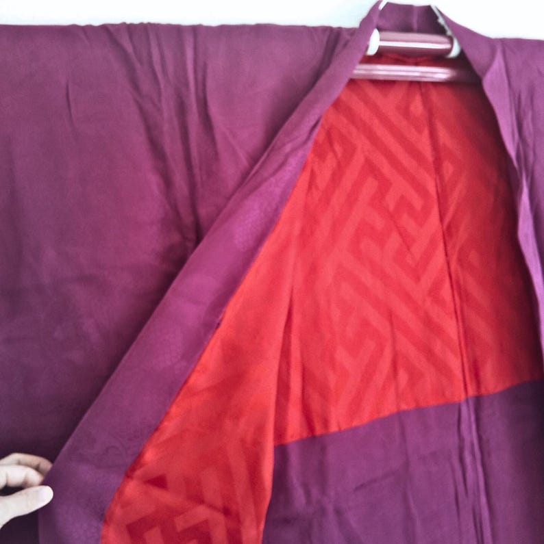 May include: A burgundy kimono with a red geometric pattern lining. The kimono is made of a soft, silky fabric.