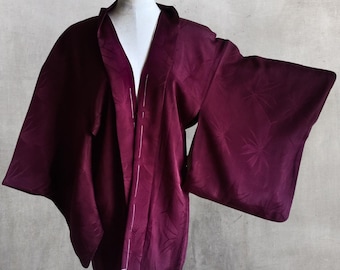 Op de afbeelding: Een diep bordeauxrode kimono-achtige jas met wijde mouwen, getoond op een mannequin. De jas heeft een subtiel bladerpatroon en een open voorkant. De stof lijkt een zacht, vloeiend materiaal te zijn.