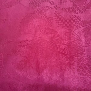 May include: A close-up of a vibrant pink fabric with a subtle embossed floral pattern. The fabric has a smooth, silky texture.