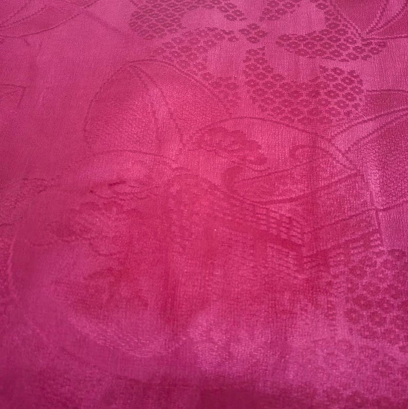 May include: A close-up of a vibrant pink fabric with a subtle embossed floral pattern. The fabric has a smooth, silky texture.