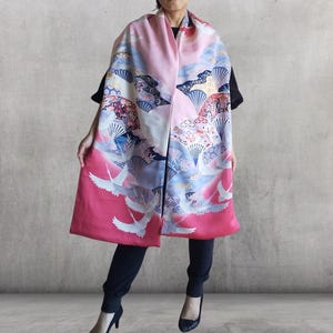 以下が含まれることがあります： ピンクと白の日本のデザインの模様の入ったスカーフ。ピンク、青、白の色合いで鶴、扇子、雲が描かれています。下端は鮮やかなピンク色です。