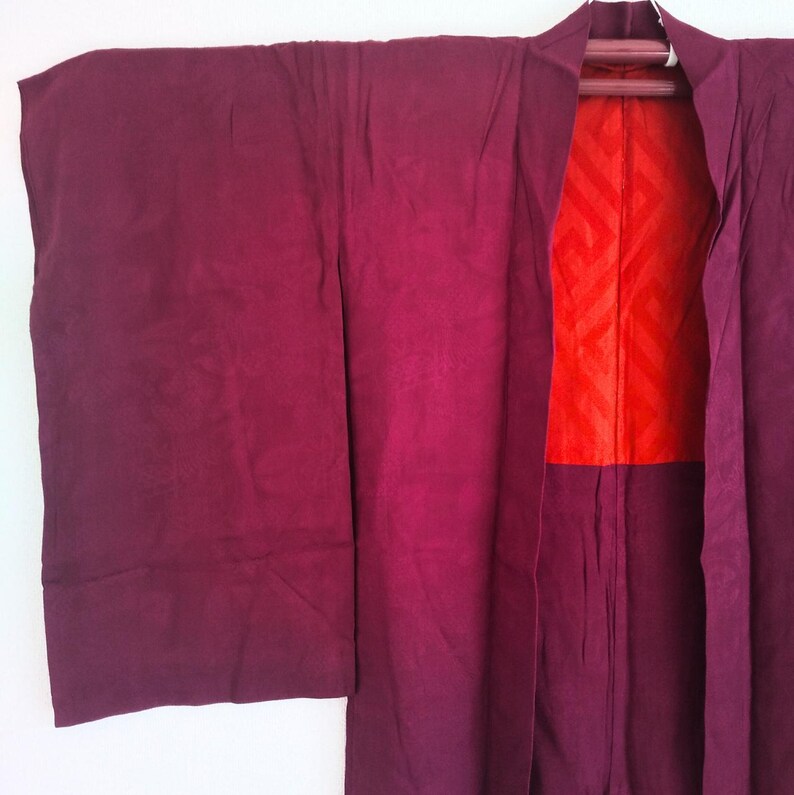 May include: A burgundy Japanese kimono with a red and white geometric pattern lining. The kimono is made of a soft, silky fabric and has a traditional design.