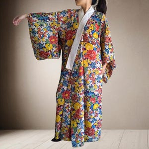 以下が含まれることがあります： 白襟のカラフルな花柄着物。着物は、白地に赤、黄、青の花の鮮やかな模様が特徴です。袖は幅広く、着物は床までの長さです。