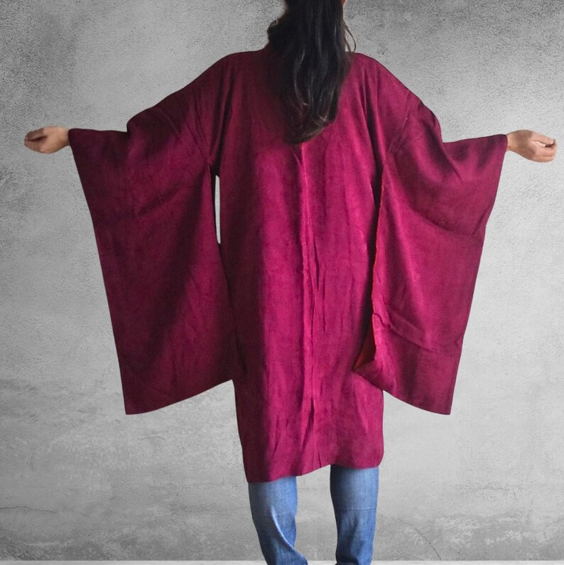 May include: A long, burgundy kimono with wide sleeves. The kimono is made of a soft, flowing fabric and has a simple, elegant design.