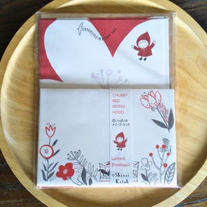 May include: A set of three red and white envelopes with a whimsical illustration of a girl in a red riding hood. The envelopes feature a floral design and the text "Right out of a fairy tale", "Chubby Red Riding Hood", "Flowers and a Merry-Go-Round", "Letter 6", "Envelopes 3", and "Shinzi Katoh".