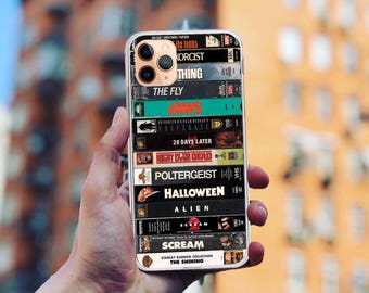 May include: A clear phone case with a collage of horror movie VHS tapes. The tapes include titles like "The Fly", "Jaws", "Poltergeist", "Halloween", "Alien", and "Scream". The case also features the Stanley Kubrick Collection: "The Shining".