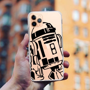May include: A clear phone case with a black and white illustration of R2-D2, a robot from the Star Wars franchise. The case has a gold trim and a camera lens cutout.