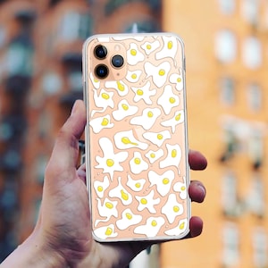 Könnte beinhalten: Eine transparente Handyhülle mit einem weißen und gelben Design aus Spiegeleiern. Die Hülle ist für ein iPhone konzipiert.