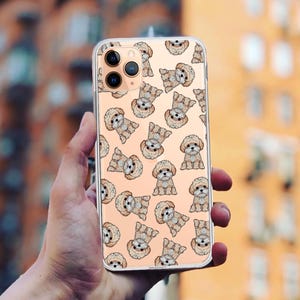 Könnte beinhalten: Eine transparente Handyhülle mit einem Muster aus kleinen braunen Hunden auf hellrosa Hintergrund. Die Hülle ist für ein iPhone mit einer Dreifachkamera konzipiert.