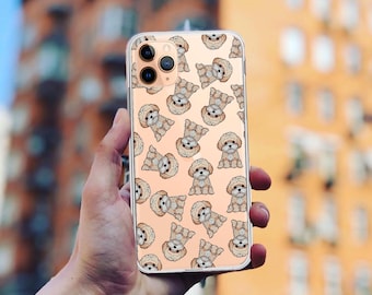Può includere: Una custodia per telefono trasparente con un motivo di piccoli cani marroni su uno sfondo rosa chiaro. La custodia è progettata per un iPhone con una fotocamera a tre obiettivi.