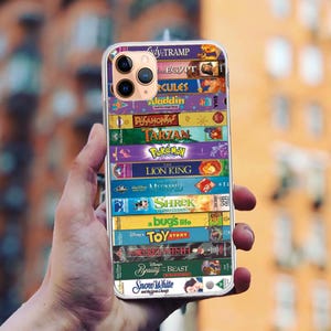 Può includere: Una custodia per telefono trasparente con un collage di copertine di VHS di film Disney. Le copertine includono La Signora e lo Vagabondo, Il Re Leone, Aladdin, Hercules, Tarzan e altro ancora.