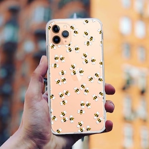 Può includere: Una custodia per telefono trasparente con un motivo di api gialle e nere su uno sfondo rosa chiaro. La custodia è progettata per un iPhone.