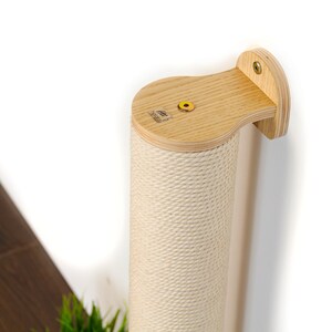 May include: A beige sisal-covered scratching post for cats, mounted to a wall with a wooden bracket. The post is made of wood and has a natural finish.