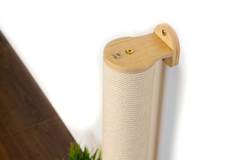 May include: A beige sisal-covered scratching post for cats, mounted to a wall with a wooden bracket. The post is made of wood and has a natural finish.