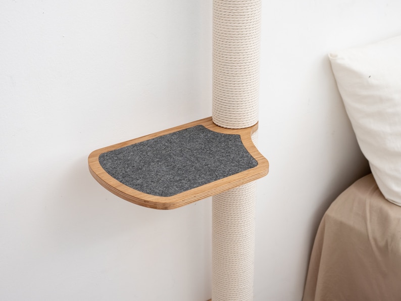 Pode incluir: Uma &aacute;rvore para gatos de madeira com uma plataforma de feltro cinza presa ao lado. A &aacute;rvore &eacute; envolvida em corda branca e est&aacute; contra uma parede branca.