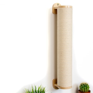 May include: A wall-mounted cat scratching post made of natural wood with a beige rope covering. The post is mounted to a white wall with a single screw.