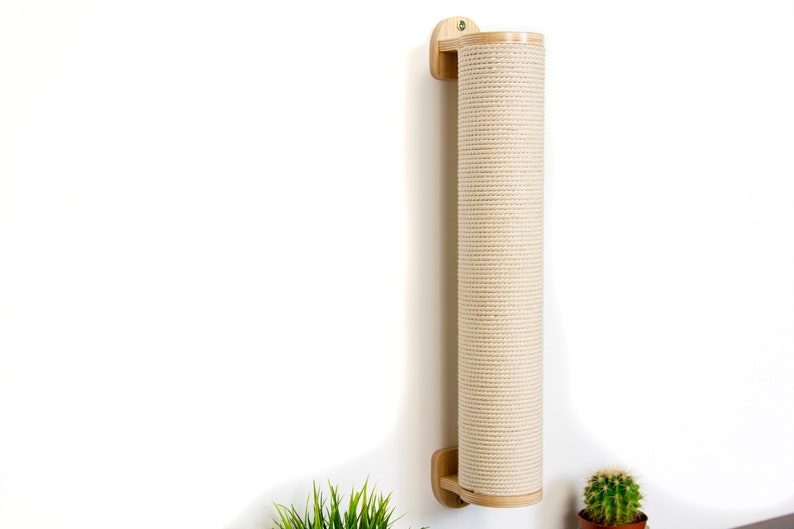 May include: A wall-mounted cat scratching post made of natural wood with a beige rope covering. The post is mounted to a white wall with a single screw.