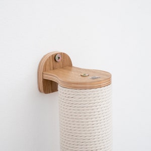 Pode incluir: Um poste de arranhar para gatos de madeira com uma cobertura de corda natural. O poste &eacute; montado em uma parede com um suporte de madeira. O suporte tem um parafuso e uma arruela.