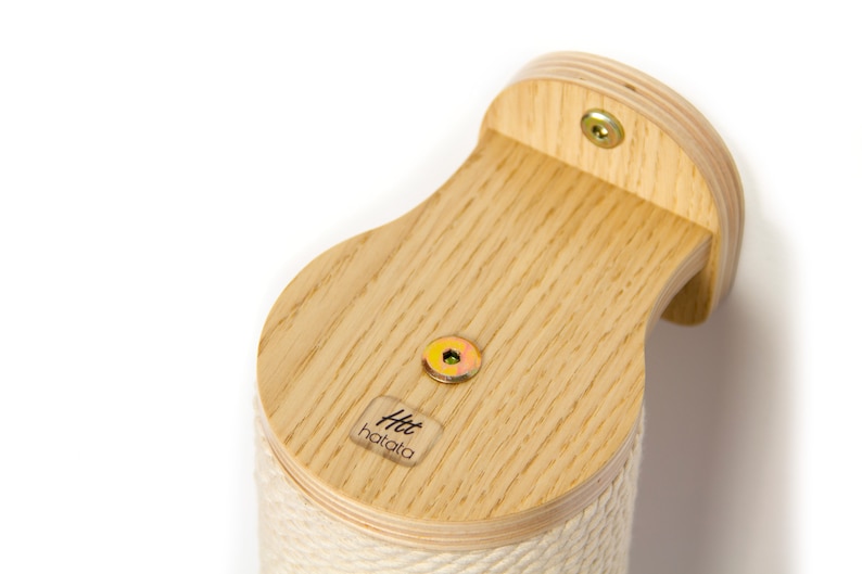 May include: A wooden cat scratching post with a natural wood finish and a beige rope covering. The post is mounted to a wall with two screws. The post has a small label with the text "Htt hatata" on the side.