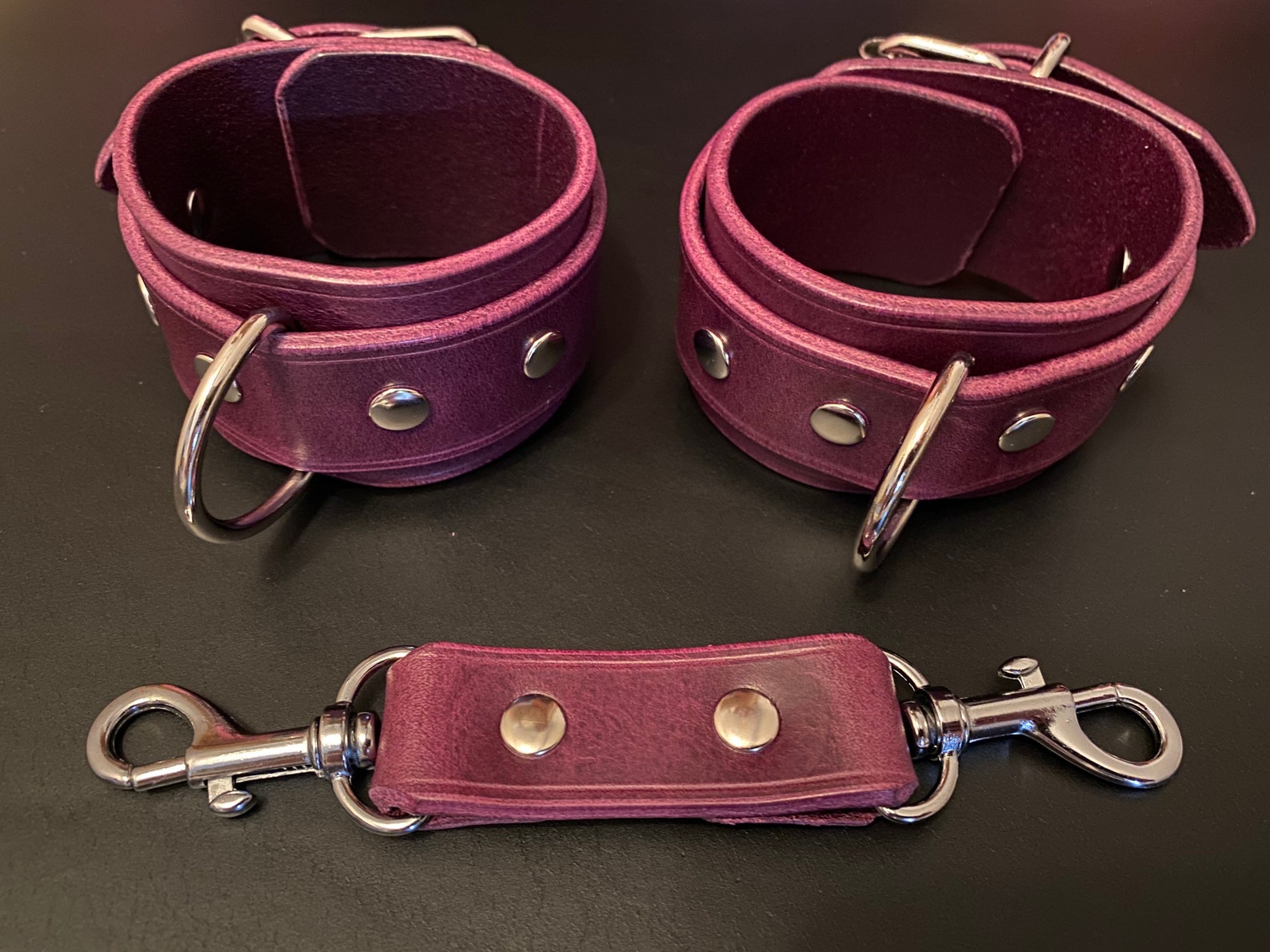 Purple leather BDSM wrist cuffs with silver fittings and leather coupler, perfect bondage restraints for tie-up sex.