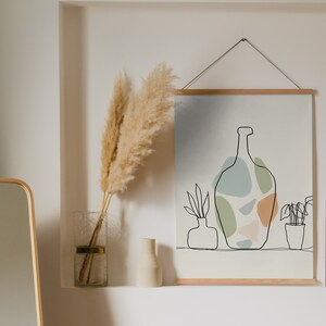 May include: A room interior with framed abstract art prints and a clothes rail. The art includes line drawings of a vase, plants, and faces, with a muted colour palette. A full-length mirror and decorative pampas grass in a vase are also visible.