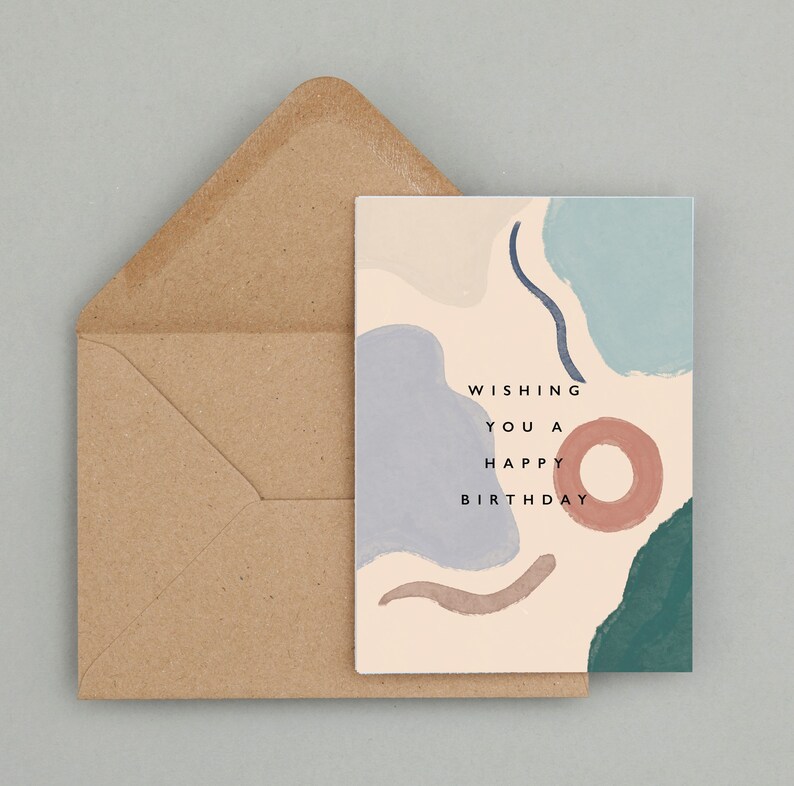 May include: A birthday card featuring abstract shapes in blue, teal, and brown, with the message "Wishing You a Happy Birthday." The card is accompanied by a brown envelope, ideal for sending birthday greetings.