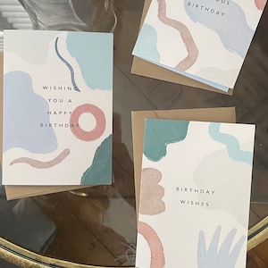 May include: Three birthday cards with abstract pastel designs. Each card has a brown envelope. The cards feature phrases such as "Wishing You a Happy Birthday" and "Have a Fabulous Birthday."
