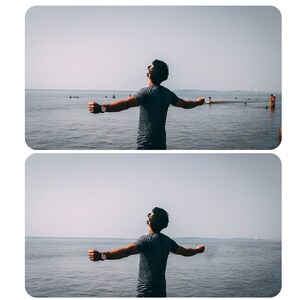 May include: A person stands with arms outstretched on a beach, facing the ocean. The water is calm and the sky is clear.